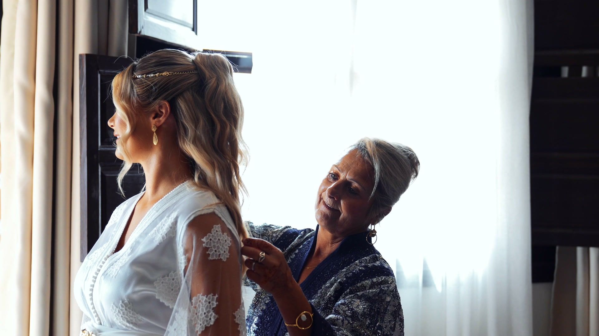 Mother helping the bride get ready by the window