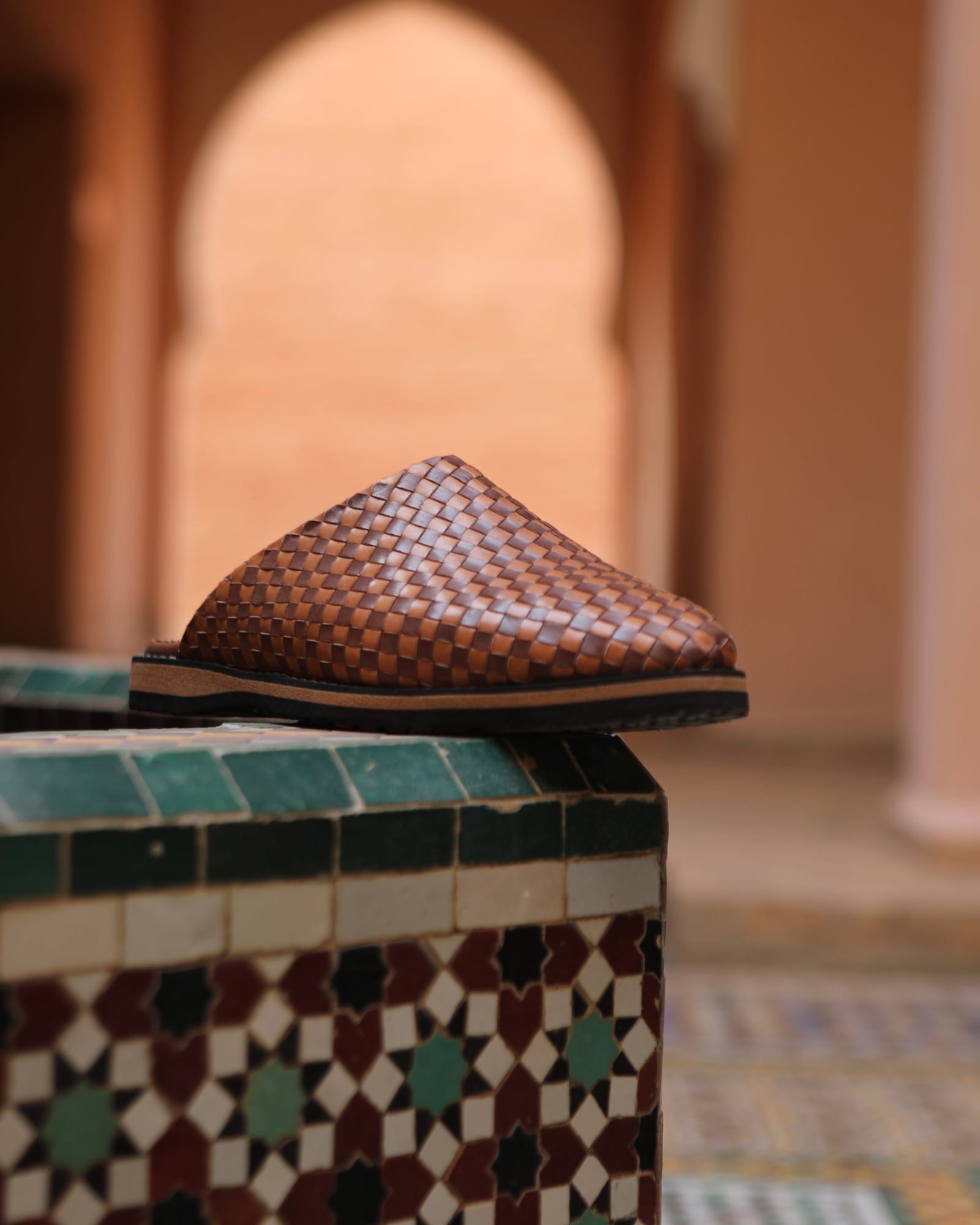 Woven leather slipper on a zellige-tiled ledge